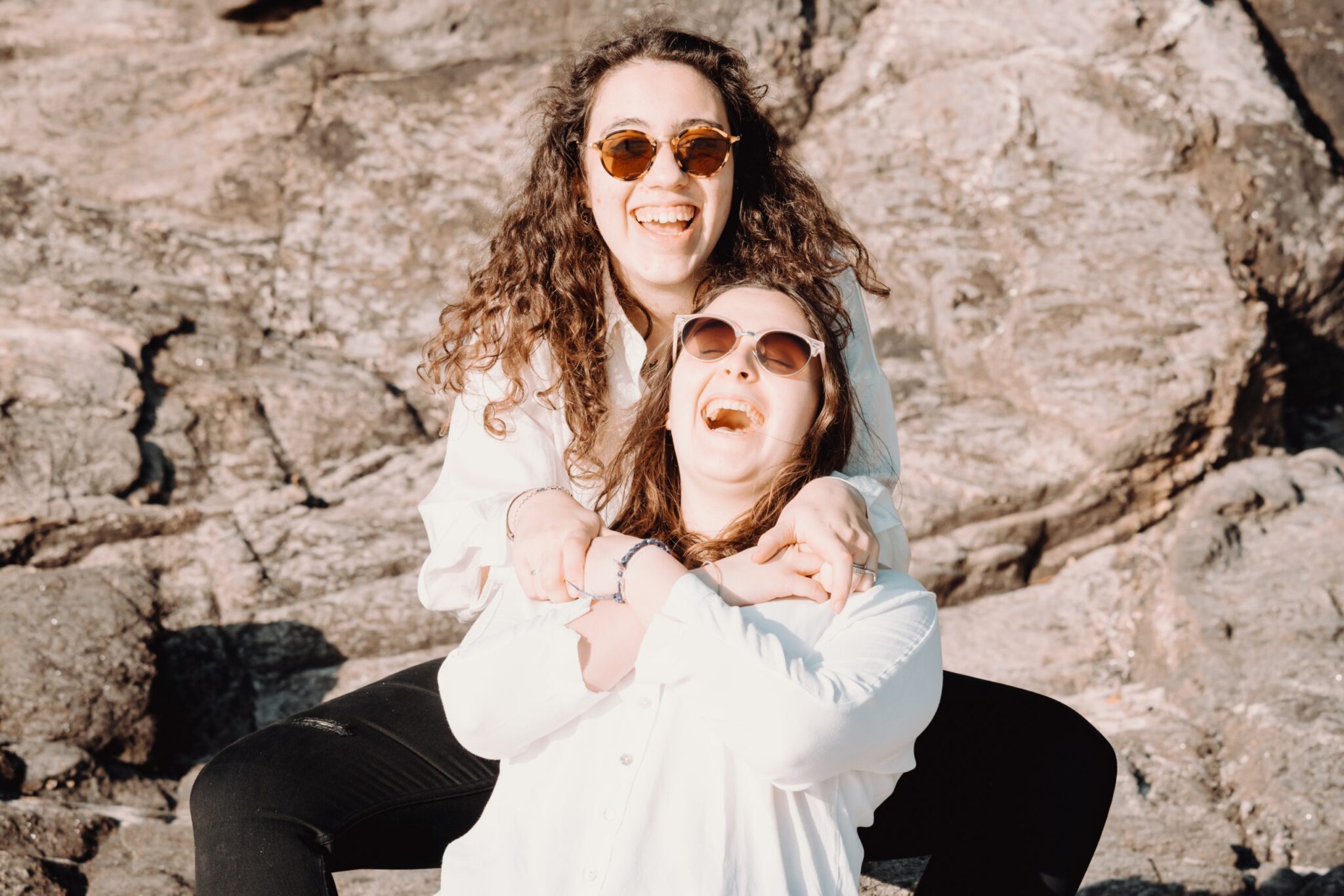 two-people-in-sunglasses-sit-in-front-of-a-large-brown-rock-scaled